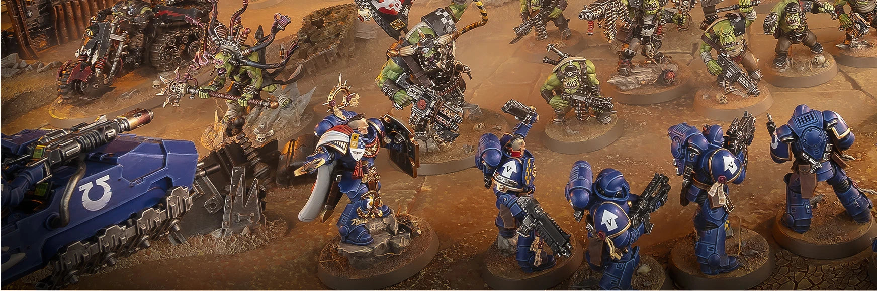 A tabletop miniature gaming scene showing multiple painted sci-fi warrior figures and a blue tank on a dusty brown battlefield terrain.