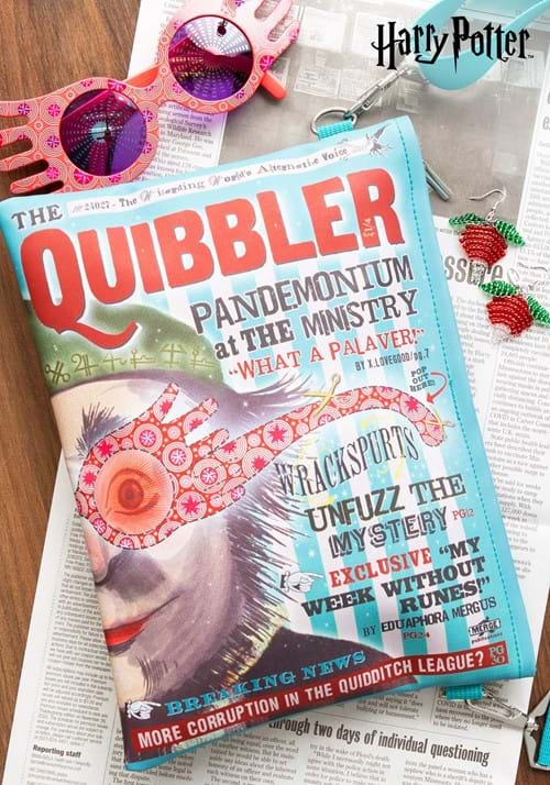 Magazine cover of 'The Quibbler' from Harry Potter series on a wooden surface with sunglasses and other items.